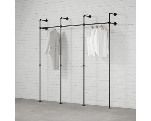 Industrieel kledingreksysteem van zwarte metalen buizen, wand- en vloermontage, driedelig, met hangende kleding voor een bakstenen muur.