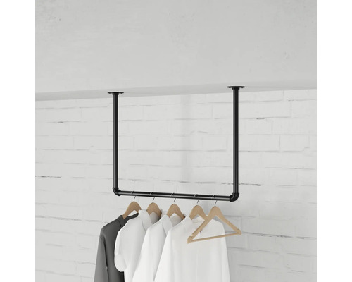 Aan het plafond gemonteerde kledingroede van metalen buizen in industrieel design met kledinghangers voor een bakstenen muur.