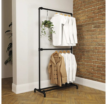 Tweelaags kledingrek van zwarte metalen buizen in industriële stijl voor een bakstenen muur, met witte kleding en een hangplant.