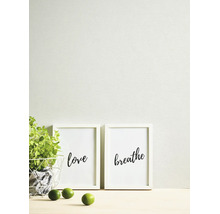 Helder ingerichte scène met structuurbehang, twee witte fotolijsten met teksten love en breathe, een groene plant en limoenen.