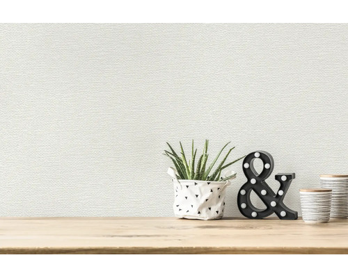 Behang met structuur en een fijn horizontaal patroon achter een plant en decoratie op een houten oppervlak in een lichte kamer.