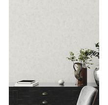 Vliesbehang met fijne pleisterstructuur op een muur achter een donker dressoir met decoratie en een plant.