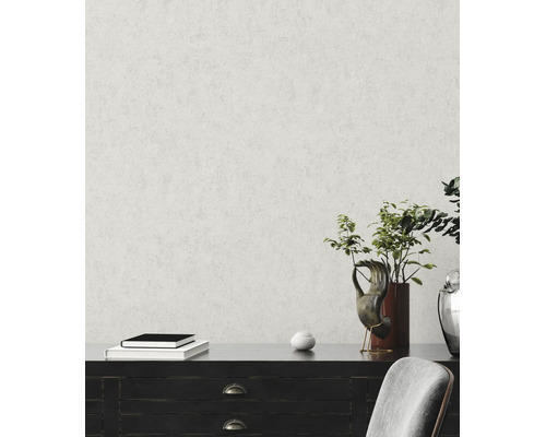 Vliesbehang met fijne pleisterstructuur op een muur achter een donker dressoir met decoratie en een plant.