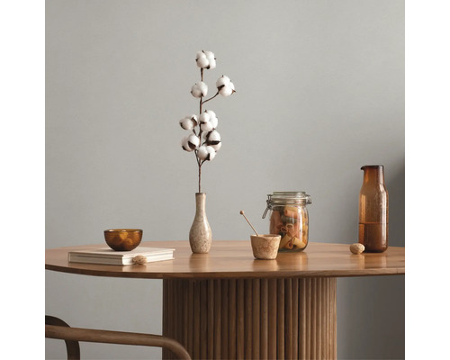 Interieurvoorbeeld met een katoentak in een vaas op een ronde houten tafel met geribbelde voet, voorraadpotten en een glazen fles.