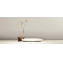 Minimalistische scène met een wit rond podium, een slanke goudkleurige vaas met decoratieve takken en een kleine bruine gaasstoel voor een getextureerde wand.