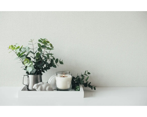 Woonruimte met wit structuurbehang, gedecoreerd met eucalyptus takken in een metalen kan en een brandende kaars op een dienblad.