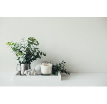 Decoratieve opstelling op een dienblad met eucalyptus takken in een metalen beker, een brandende kaars in glas en een keramisch konijnenfiguurtje.