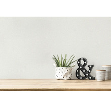 Wit gestructureerd vliesbehang op een muur boven een licht houten tafel met een plant en decoratieve elementen.
