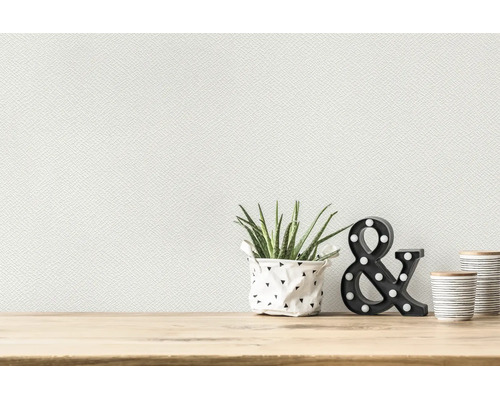 Wit gestructureerd vliesbehang op een muur boven een licht houten tafel met een plant en decoratieve elementen.