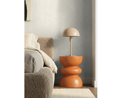 Paddenstoelvormige tafellamp op een moderne, sculpturale bijzettafel naast een bed met een getextureerd hoofdbord.