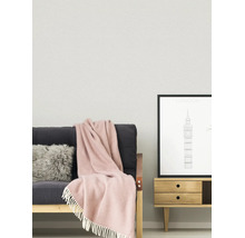 Lichte, georganiseerde woonkamer met gestructureerde wand, een bank met bontkussen en deken met franjes en een houten bijzettafel met poster.
