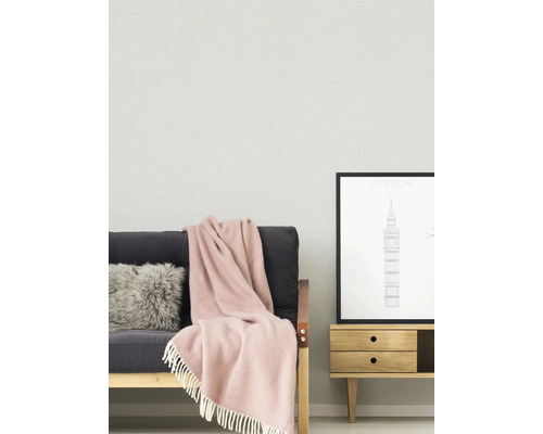 Lichte, georganiseerde woonkamer met gestructureerde wand, een bank met bontkussen en deken met franjes en een houten bijzettafel met poster.