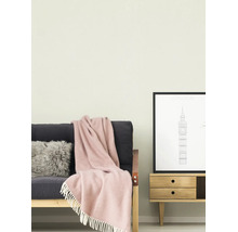 Licht geschilderde muur in een woonkamer met een donkere bank, een roze wollen deken met franjes en een houten dressoir met een poster van Londen.