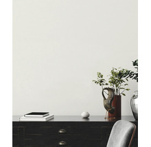 Wit behang met structuur op een muur achter een donker bureau met decoratieve voorwerpen.