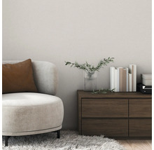 Moderne woonkamer met gestructureerde wandafwerking, een beige fauteuil met bruin kussen en een donkerhouten ladekast.