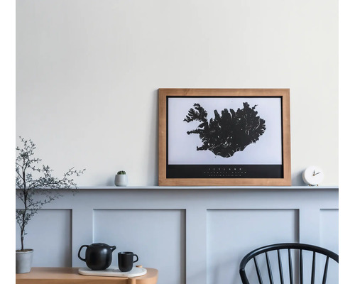Houten fotolijst met kaart van IJsland op een wandplank in een lichte kamer met wandpanelen.
