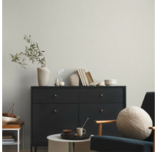 Licht vliesbehang met fijne structuur achter een donkere commode in een modern ingerichte woonkamer.