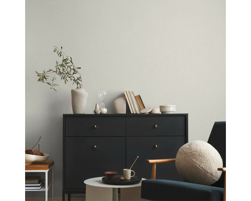 Licht vliesbehang met fijne structuur achter een donkere commode in een modern ingerichte woonkamer.
