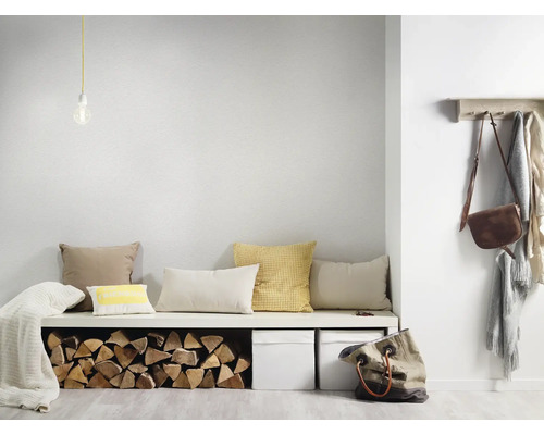 Lichte minimalistische hal met een witte bank, diverse kussens, een opslag voor haardhout, twee witte boxen en een houten kapstok.