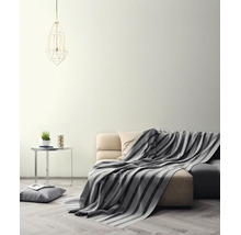 Lichte woonkamer met crèmekleurige muur, bank met gestreepte deken, bijtafel en geometrische hanglamp op een parketvloer.