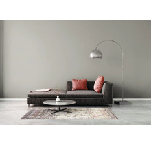 Moderne woonkamer met grijze muur, donkere bank, booglamp en marmeren salontafel op een patroontapijt en betonnen vloer.