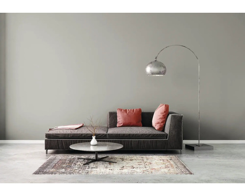 Moderne woonkamer met een donkere stoffen bank, rode kussens, een ronde marmeren salontafel, een gedessineerd tapijt en een zilveren booglamp.