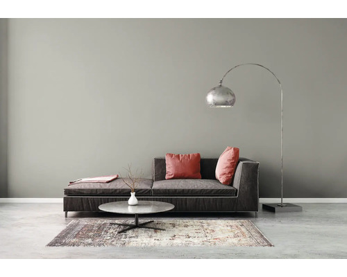Moderne woonkamer met donkergrijze bank, booglamp, ronde salontafel en een gedessineerd vloerkleed tegen een grijze wand.