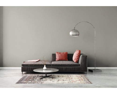 Moderne woonkamer met grijze muur, donkergrijze bank, rode kussens, zilveren booglamp en ronde salontafel op een gedessineerd tapijt.