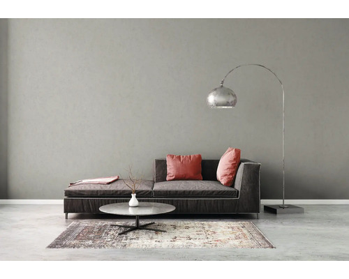 Moderne woonkamer met donkere bank, roze kussens, ronde stenen salontafel, zilveren booglamp en een patrijstapijt tegen een grijze muur.