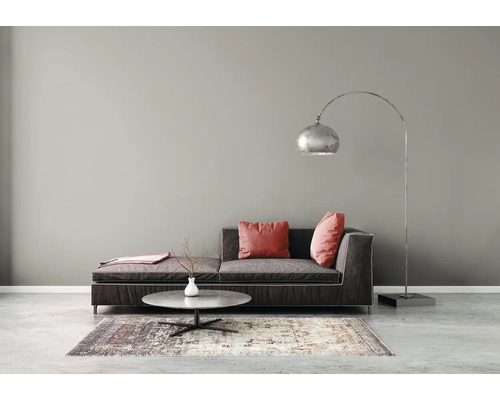 Moderne woonkamer met grijze muurverf, donkere stoffen bank, lage ronde salontafel, gemêleerd tapijt en een grote booglamp van metaal.