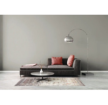 Moderne woonkamer met donkergrijze bank, rode kussens, zilveren booglamp, ronde salontafel en gedessineerd vloerkleed tegen een grijze muur.