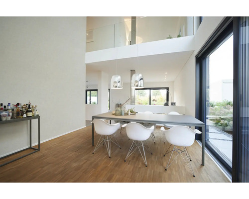 Moderne lichte eetkamer met grote grijze tafel, witte designstoelen, chromen hanglampen en houten vloer bij een glazen schuifpui.