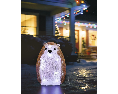 Staande egel van acryl, koudwit verlicht, winterse buitenversiering in een besneeuwde tuin voor een verlicht huis.