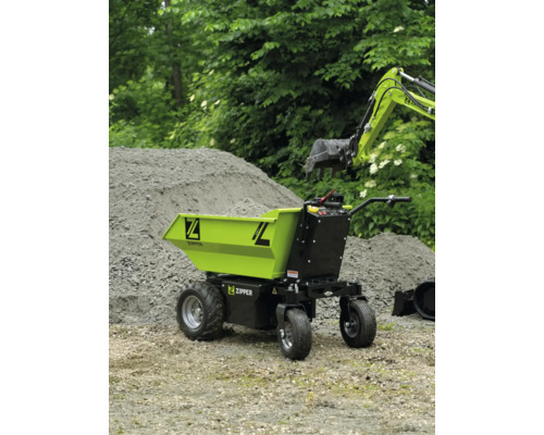 Zipper elektrische kruiwagen op een bouwplaats bij een hoop zand en een graafmachine-arm.
