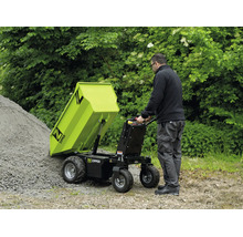 Een man leegt een Zipper motorkruiwagen met kiepmechanisme op een grindhoop in de tuin. Functionele, lichte buitenomgeving. Zipper Logo.