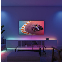 Moderne woonkamer met een televisie aan de wand die een raceauto toont, LED-sfeerverlichting achter de meubels en een glazen tafel.
