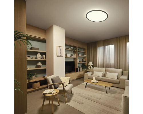 Lichte, georganiseerde woonkamer met ronde LED-plafondlamp, bank, houten planken, salontafel en vloerkleed.