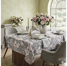 Gedekte eettafel met tafelkleed met bloemenpatroon, vierkant servies, een boeket bloemen en een kandelaar in een lichte eetkamer.