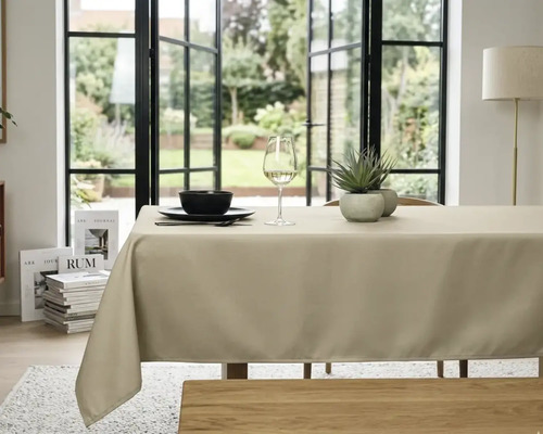 Beige tafelkleed op een eettafel in een lichte, georganiseerde kamer met grote glazen deuren en uitzicht op de tuin.