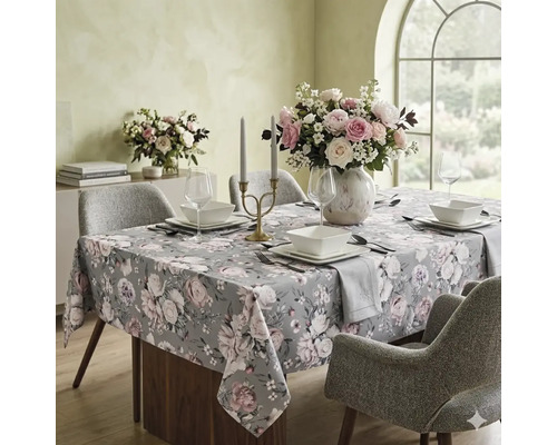 Gedekte eettafel met tafelkleed met bloemenpatroon, vierkant servies, een boeket bloemen en een kandelaar in een lichte eetkamer.