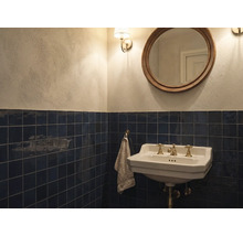 Klassieke badkamer met donkerblauwe wandtegels, witte keramische wastafel met messing kranen, ronde spiegel en lichte muren.