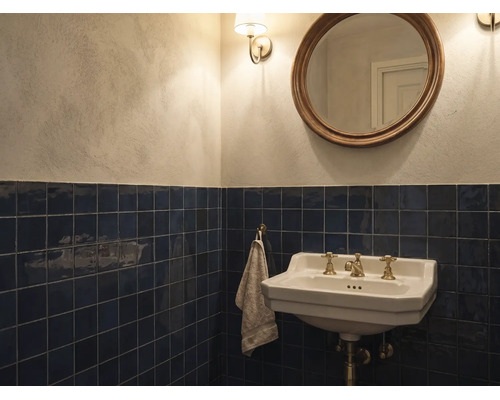 Klassieke badkamer met donkerblauwe wandtegels, witte keramische wastafel met messing kranen, ronde spiegel en lichte muren.
