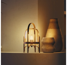 Moderne tafellamp in lantaarnvorm met glas en metaal, warm licht naast twee keramische vazen met textuur op een plank.