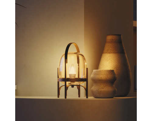 Moderne tafellamp in lantaarnvorm met glas en metaal, warm licht naast twee keramische vazen met textuur op een plank.