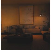Moderne woonkamer met een grote wanddecoratie, stoffen bank en een booglamp met glazen kap in een warme, gedimde sfeer.