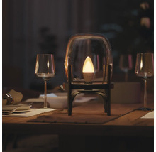 Philips Hue slimme LED kaarslamp brandt in een glazen stolp op een gedekte eettafel met wijnglazen in een gedimde kamer.