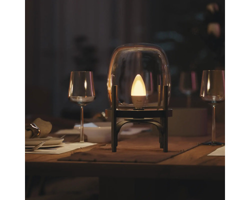 Philips Hue slimme LED kaarslamp brandt in een glazen stolp op een gedekte eettafel met wijnglazen in een gedimde kamer.