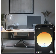Slimme lichtregeling van een bureaulamp via een smartphone-app in een modern ingericht thuiskantoor.