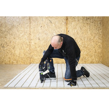 Vakman knielt op een witte vloerverwarmingsplaat en zet deze vast met elektrisch gereedschap voor een wand van OSB-platen.