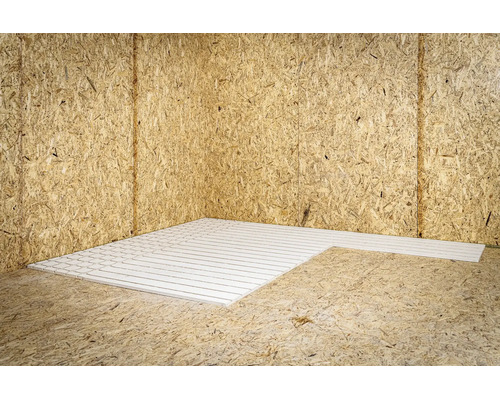 Witte systeemplaat met groeven voor vloerverwarming gelegd op OSB-platen in een hoek van de kamer.